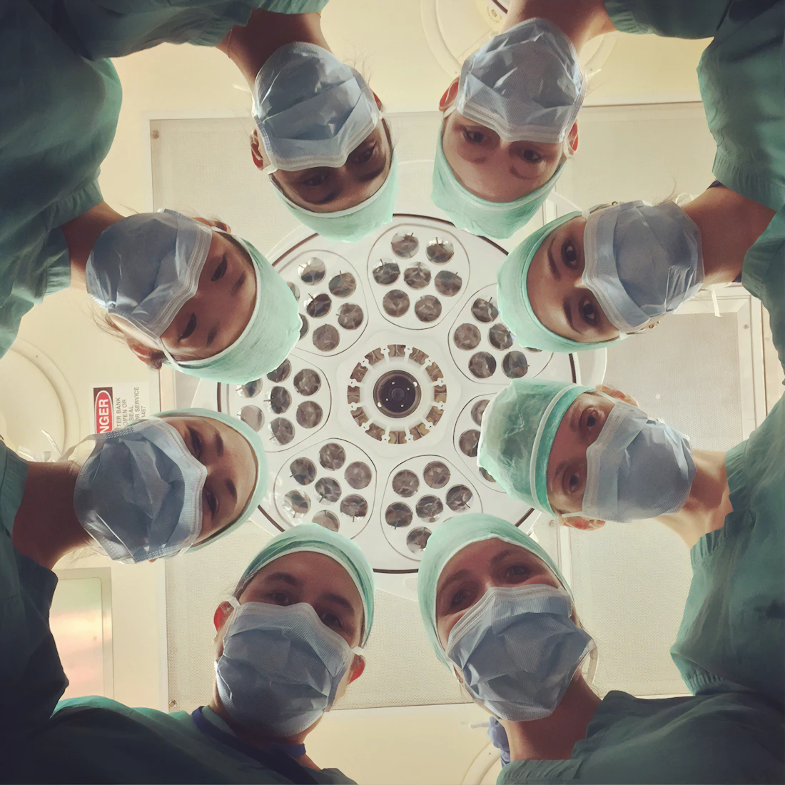 A surgical team in masks and caps looks down from under the operating light